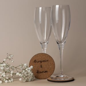 Dessous de verre en liège personnalisable avec gravure "Virginie & Karim", accompagné de deux flûtes à champagne et de gypsophile.