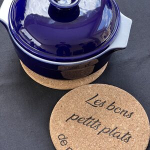 Dessous de plat en liège gravé avec l'inscription "Les bons petits plats de ma nounou", sous une cocotte en fonte bleue.